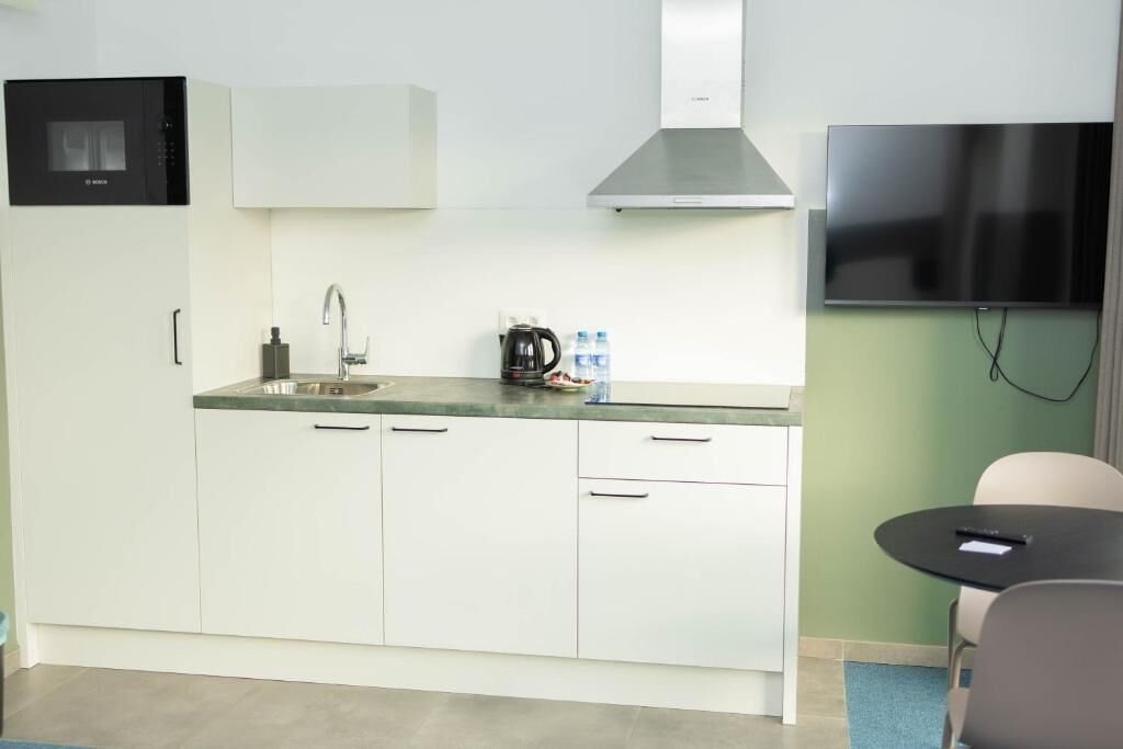 Een kleine keuken met witte kasten, een roestvrijstalen afzuigkap, een magnetron en een flatscreen televisie aan de muur.