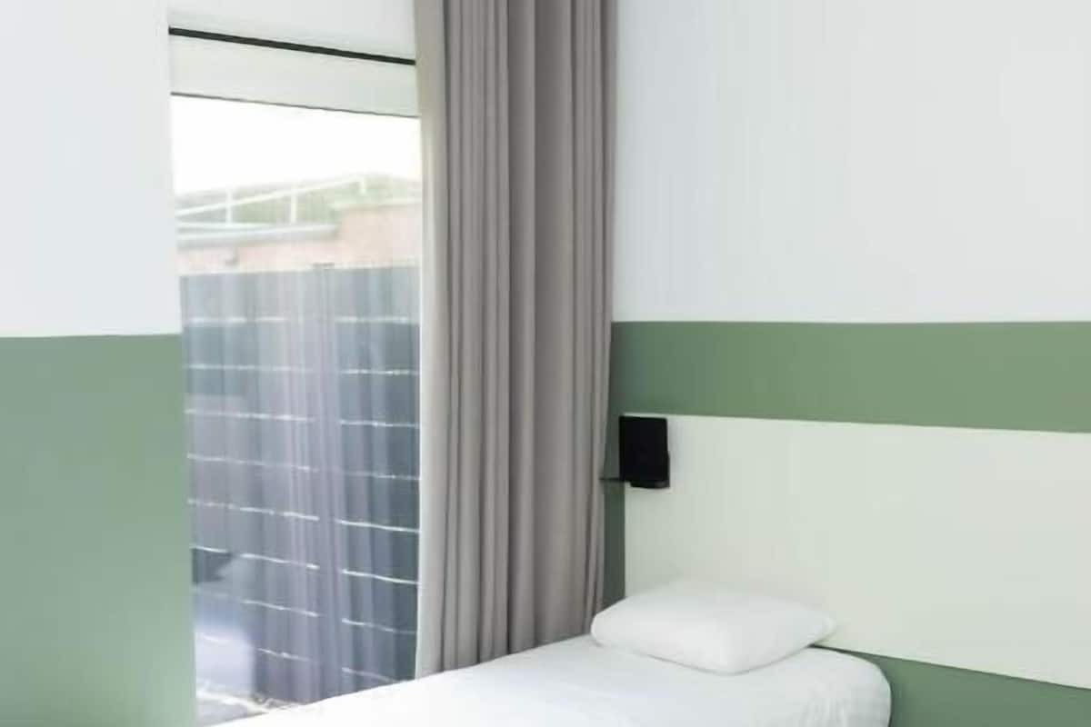 Un lit simple dans une chambre donnant sur une clôture.