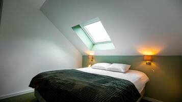 Ein Schlafzimmer mit Dachfenster, einem Bett mit dunkler Decke, zwei Nachttischlampen und einer grünen Akzentwand.