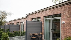 A modern building with a brick facade, numbered 13, featuring a glass door entrance and a small patio area with a table and chairs.