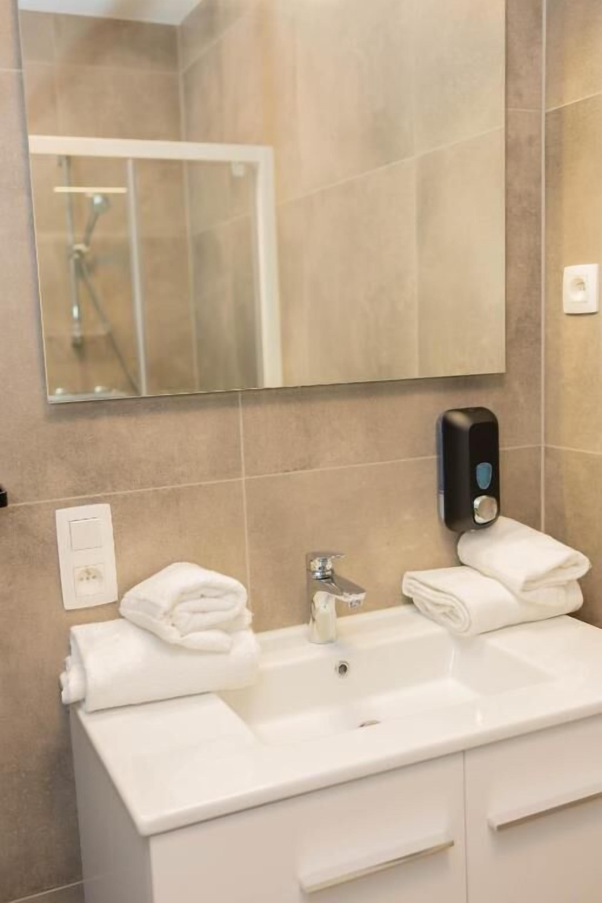 A modern bathroom with a large mirror, a sink with a soap dispenser, and two towels on the counter.