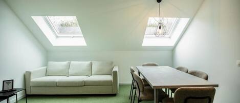 A room with a sofa, a dining table with chairs, and two skylights.