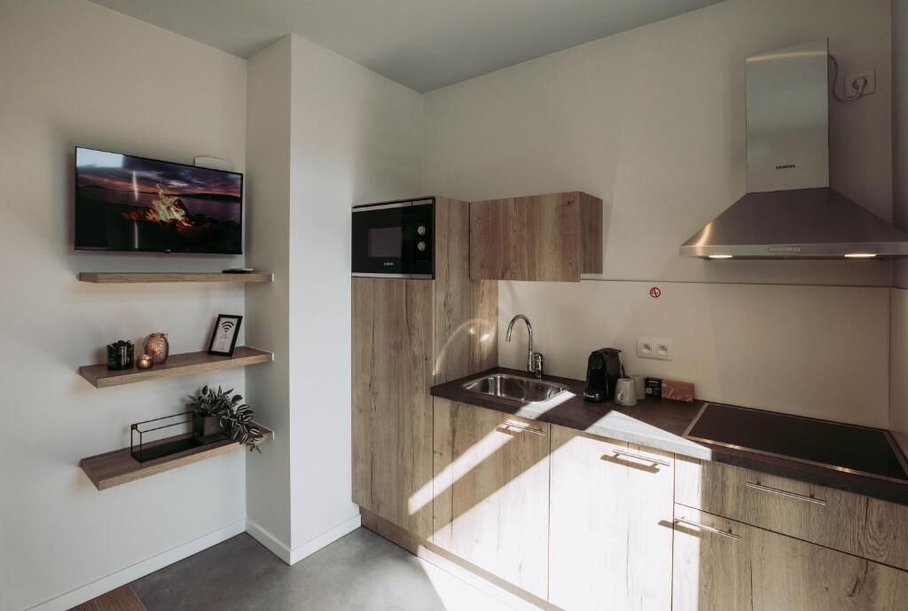 Una cocina moderna con armarios de madera, microondas empotrado, pileta de acero inoxidable y televisor de pantalla plana en la pared.