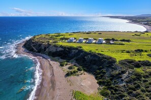 Luftaufnahme eines Anwesens an der Küste mit Strand, Ozean und einer Gruppe weißer Gebäude.