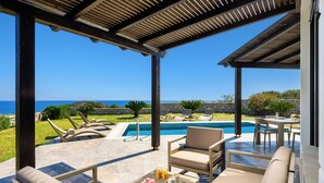 A poolside area with lounge chairs, a table with drinks, and a view of the ocean. - Aqua Natura Villas - Villa Beluga (Rhodes)