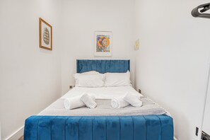 Una cama bien hecha con sábanas blancas y un cabecero azul en una habitación con paredes blancas.