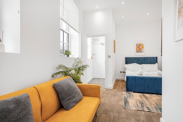 Una habitación de hotel moderna con un sofá, una cama, una planta en maceta y un cuadro en la pared.