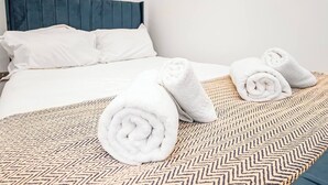 A neatly made bed with white linens, a patterned throw, and rolled towels on a chevron-patterned bedspread.