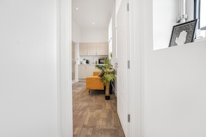 Un pasillo que conduce a una cocina con gabinetes blancos, una silla amarilla y una planta en maceta.