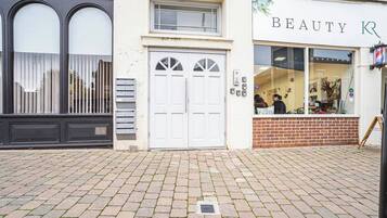 A building with a white facade, a brick entrance, and a storefront with a sign that reads 'BEAUTY R'.