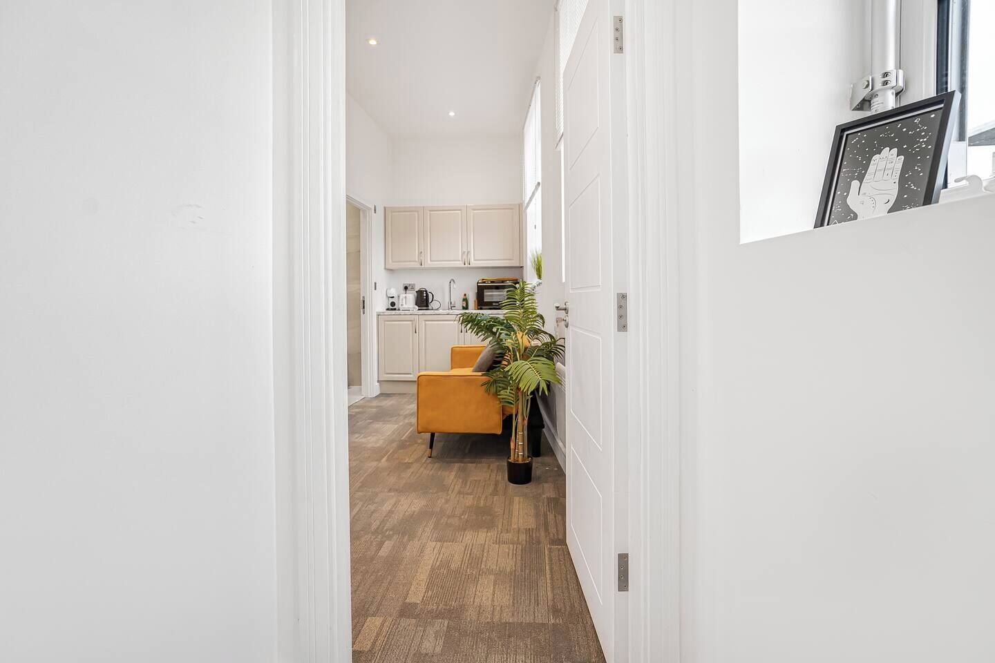 Un pasillo que conduce a una cocina con armarios blancos, una silla amarilla y una planta en maceta.