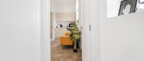 Un pasillo que conduce a una cocina con armarios blancos, una silla amarilla y una planta en maceta.