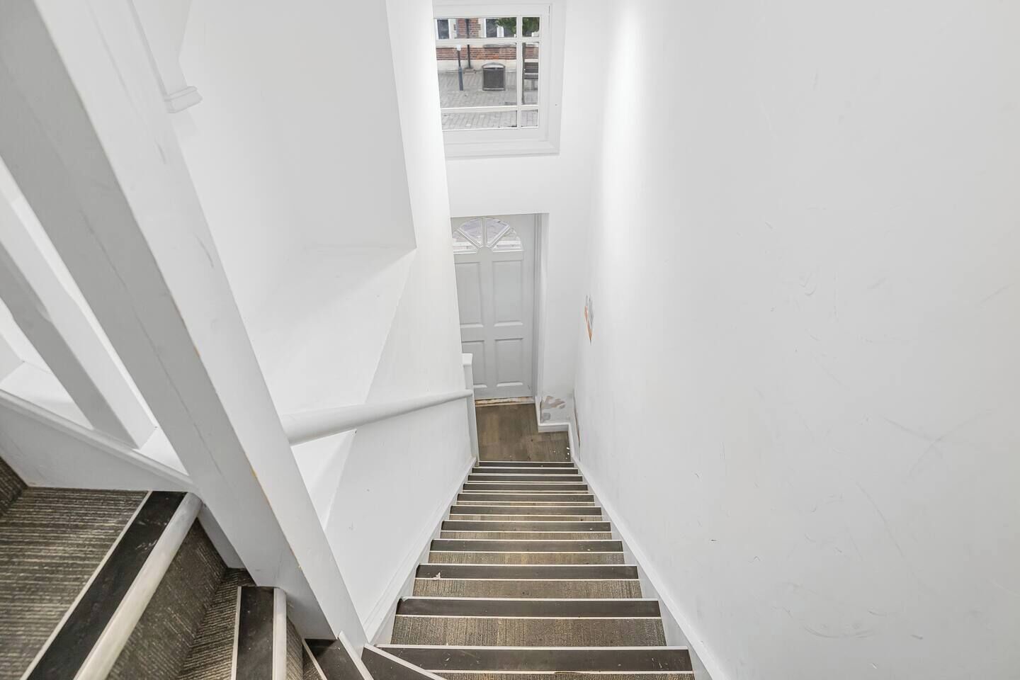 A narrow stairwell with white walls and a wooden handrail.