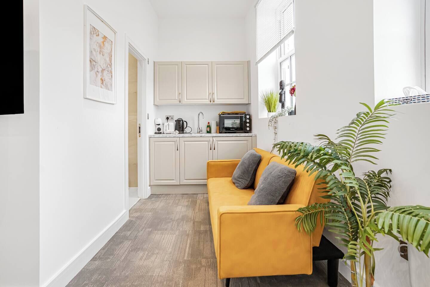Un espacio habitable compacto con kitchenette, un sofá con cojines y una planta en maceta.