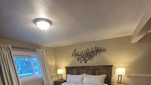 Une chambre à coucher avec un lit en bois, deux tables de chevet avec des lampes, un élément décoratif mural et une fenêtre avec des rideaux.