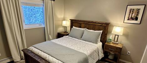 A bedroom with a bed, two bedside tables with lamps, a ceiling fan, a window with curtains, and a framed picture on the wall.