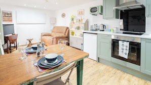 Una cocina compacta con comedor, que incluye una mesa de madera dispuesta para dos personas, un sofá y un mueble pequeño con microondas y estufa.