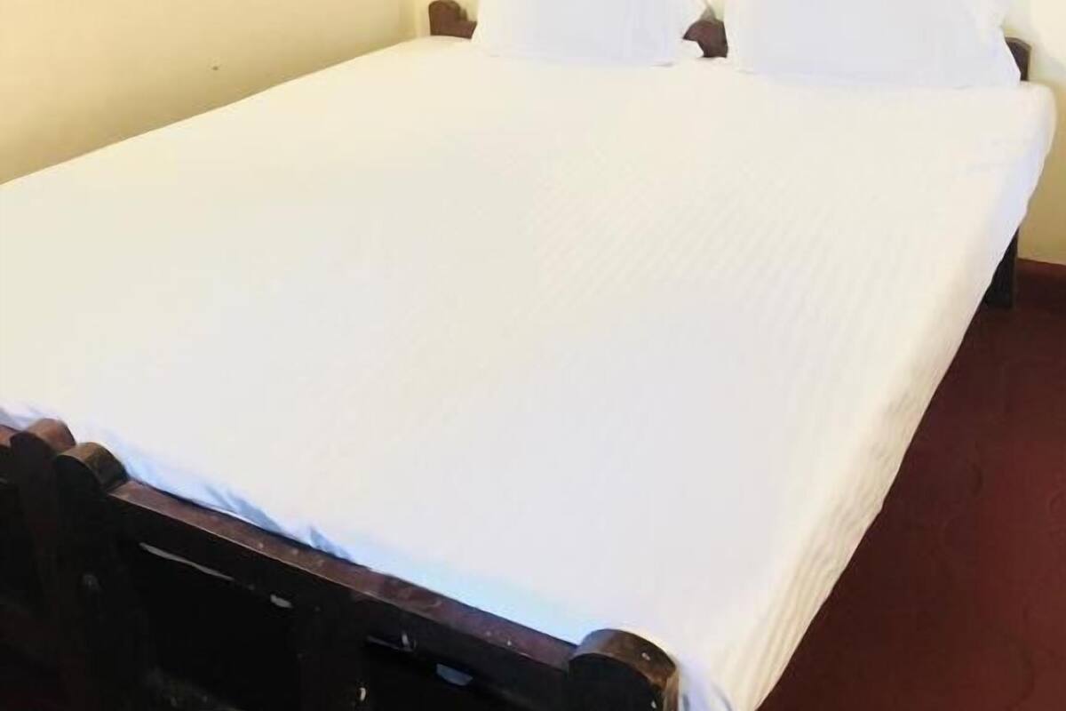 A single bed with white bedding in a room with plain walls and a wooden floor.