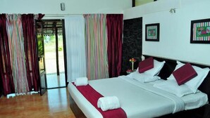 A hotel room with a large bed, striped curtains, a view of the outdoors, and a small table with a vase of flowers. - Punarjani Ayurvedic Resorts (Udumbanchola)