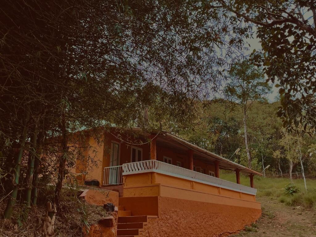 A rustic, single-story building with a balcony, surrounded by dense foliage.