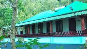 A building with a green roof and white walls, surrounded by trees. - Punarjani Ayurvedic Resorts (Udumbanchola)