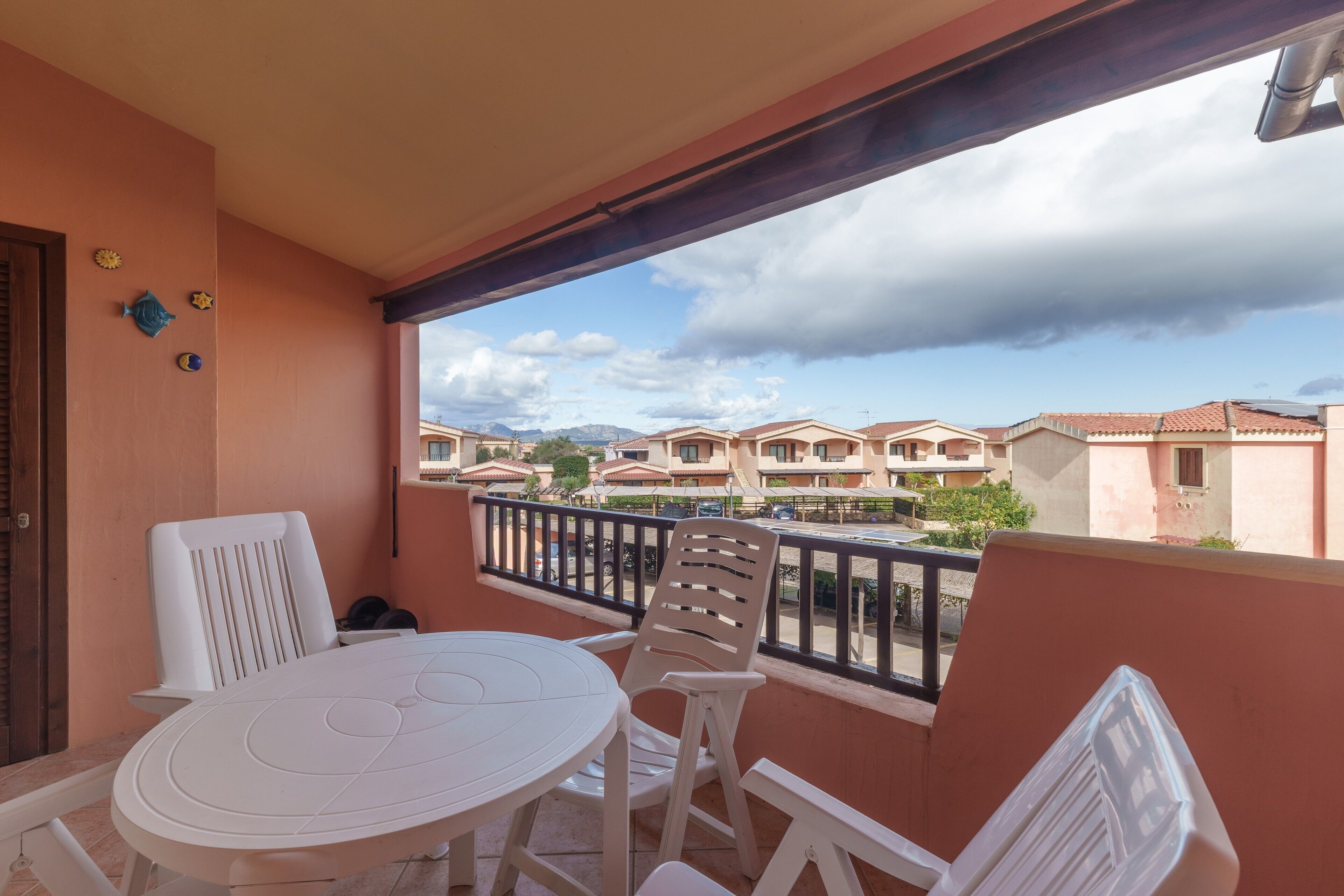 A balcony with a table and chairs, a view of neighboring buildings, and a cloudy sky.