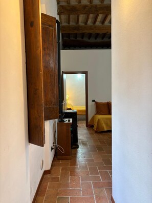 A narrow hallway with a wooden door, a small desk with a computer, and a bed with a yellow blanket. - ANCIENT LODGING MOLENDA (Città di Castello)