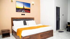 Una camera da letto con un letto di legno, biancheria da letto bianca, un quadro che raffigura un paesaggio urbano e una porta alla destra.