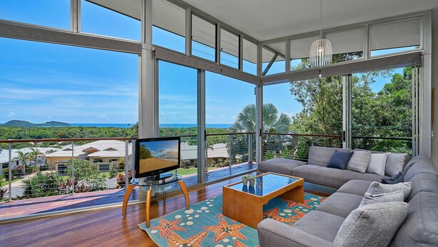 A spacious living room with a large window, a sofa, a coffee table, and a television. - Bedrock Palm Cove I Private Pool I Sea Views I Family Retreat (Cairns)