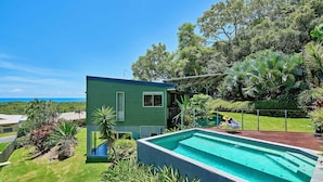 A house with a swimming pool, a covered patio, and a view of the ocean. - Bedrock Palm Cove I Private Pool I Sea Views I Family Retreat (Cairns)