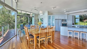 A modern kitchen with a central island, wooden dining table, and chairs. - Bedrock Palm Cove I Private Pool I Sea Views I Family Retreat (Cairns)