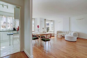 Een ruime woonkamer met een houten vloer, een eettafel met stoelen en een witte bank.