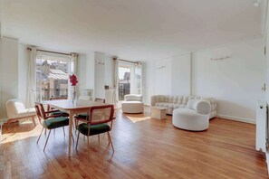 Een ruime woonkamer met houten vloer, een zithoek met tafel en stoelen, en een moderne zithoek.