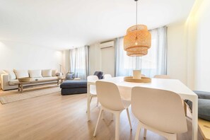 Ein modernes Wohnzimmer mit Essbereich, ausgestattet mit einem weißen Sofa, einem Holztisch und einem Esstisch mit weißen Stühlen.