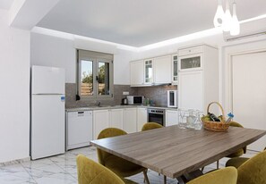 A modern kitchen with white cabinets, a wooden dining table, and yellow chairs. - Primavera Villa - 2 Heated Pools & Jacuzzis (Pagkalochori)