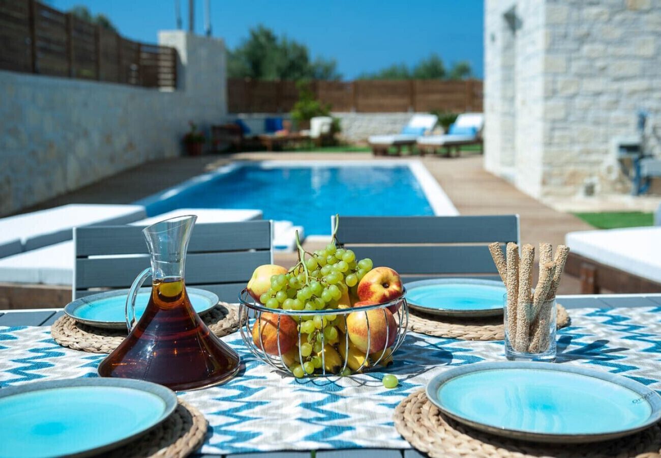 Une table placée au bord de la piscine, sur laquelle on trouve une carafe, un saladier rempli de fruits et un verre contenant ce qui semble être une boisson.