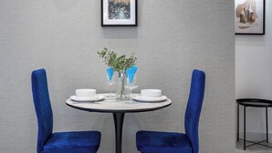 A dining area with a round table, two chairs, a vase with flowers, and two framed pictures on the wall.