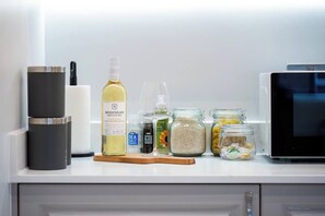 Een keukenblad met een wijnfles, zoutvaatje, kruidenmolen en potten met ingrediënten.