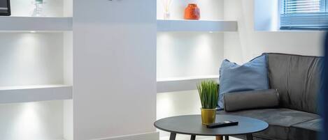 A modern living room with a grey sofa, a round coffee table with a plant, and a flat-screen TV mounted on the wall.