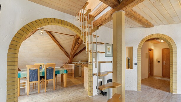Una habitación amplia con pisos de madera, un comedor con sillas y una mesa, una escalera y una zona de cocina.