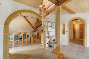 Een ruime kamer met houten vloeren, een eethoek met stoelen en een tafel, een trap en een keuken.