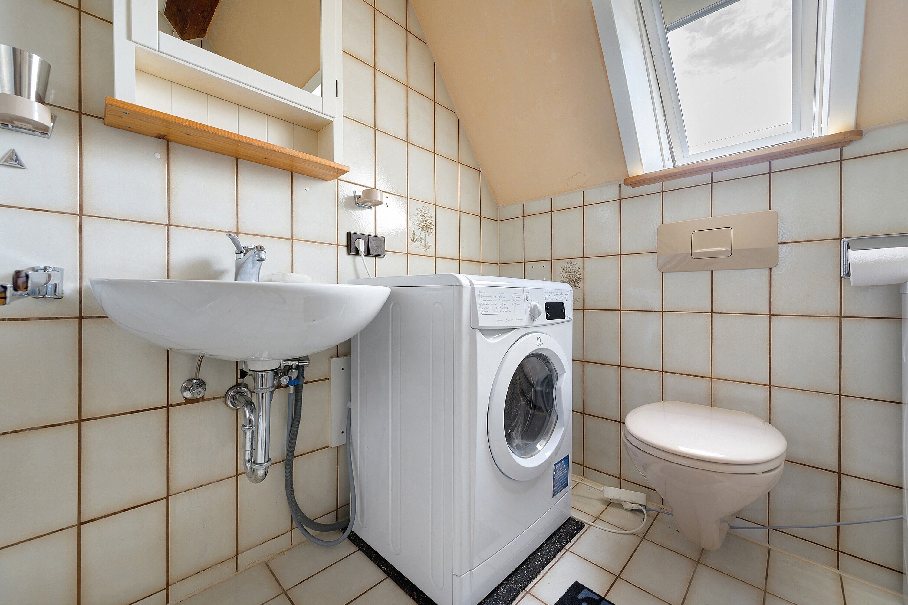 A compact bathroom with a washing machine, a toilet, and a sink.