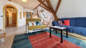 Un espacio tipo loft con vigas de madera a la vista, un sofá, una mesa y una alfombra colorida.