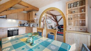 Una cocina con armarios de madera, una mesa de comedor con mantel a cuadros y un aparador empotrado con cristalería.