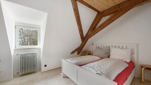 Un dormitorio con techo inclinado, un radiador blanco, estructura de cama de madera y una ventana.