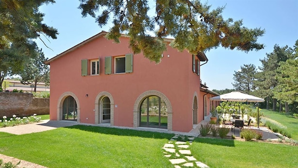 A pink villa with a stone pathway leading to the entrance, surrounded by a well-maintained lawn and a garden area with outdoor furniture. - Apartment Azzurro- Cignella Resort Tuscany (Trequanda)