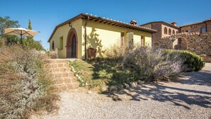 A rustic building with a stone staircase leading to a door, surrounded by dry vegetation and a clear sky.
