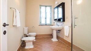 Un bagno con due servizi igienici, un lavabo, una finestra con tende e uno spazio doccia.