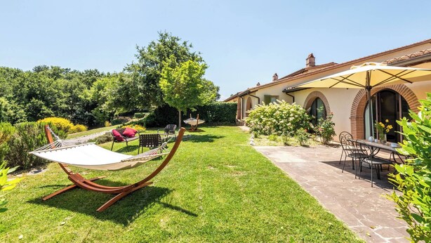 A well-maintained garden with a hammock, a patio table with chairs, and a building with arched windows. - Villa Aquila-cignella Resort Acommodation Tuscany (Trequanda)