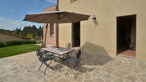 Eine Terrasse im Freien mit Tisch, Stühlen und einem Sonnenschirm, vor einer Backsteinmauer.